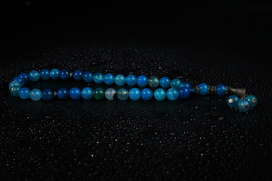 Blue agate tasbih glowing on dark surface with droplets