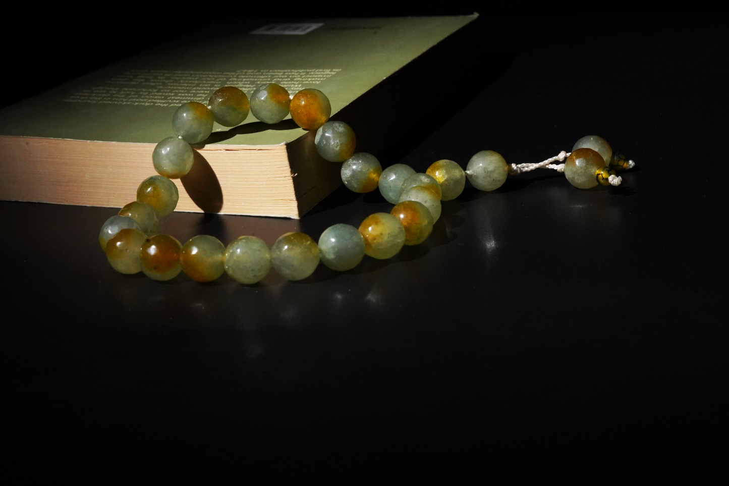 Stone tasbih on a dark surface with a book in the background