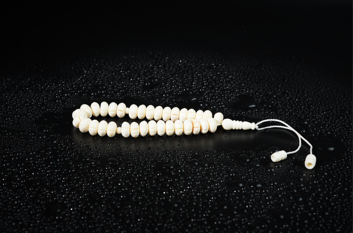 Camel bone tasbih on dark textured backdrop with droplets