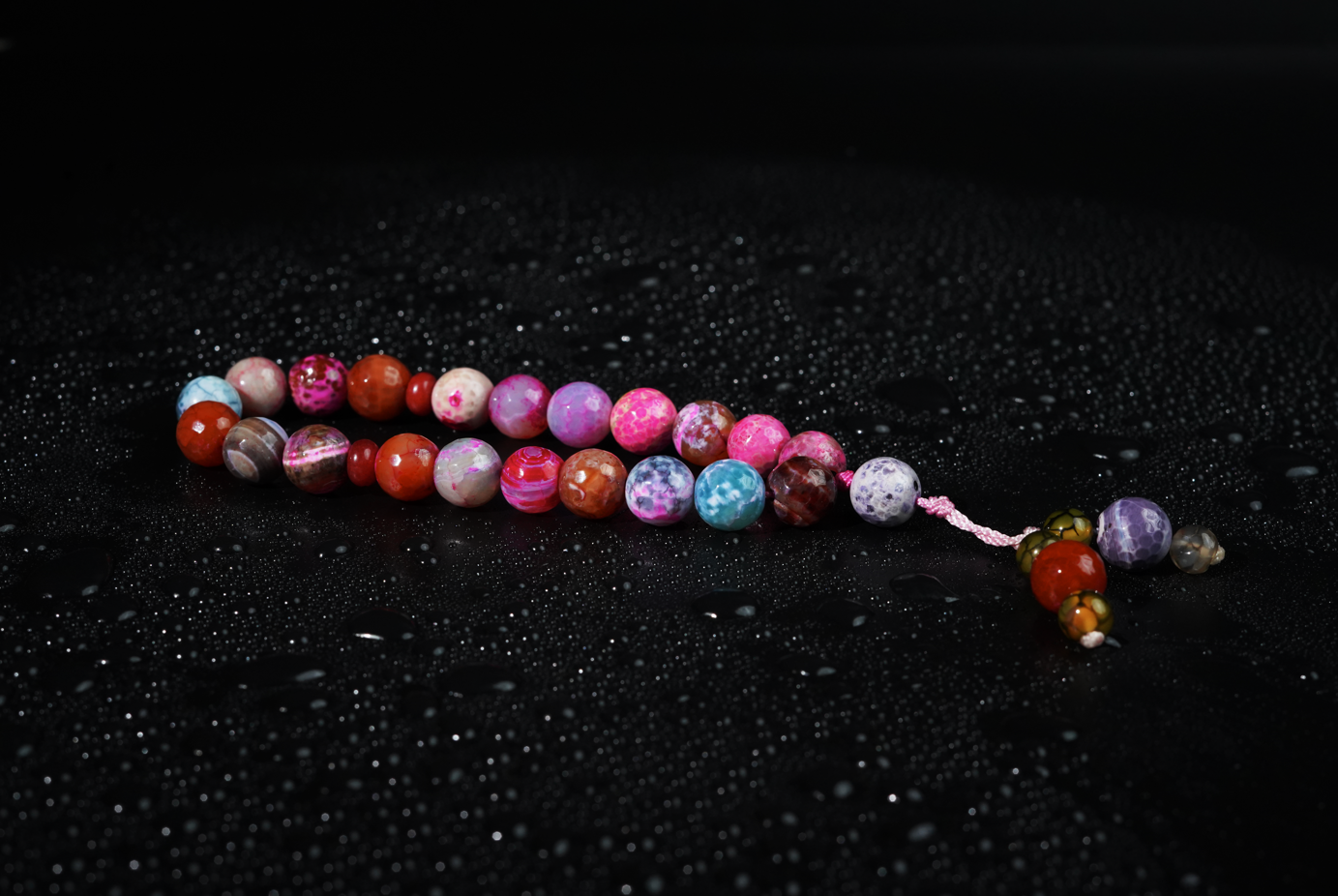 Aurora agate tasbih on matte black background with subtle water droplets