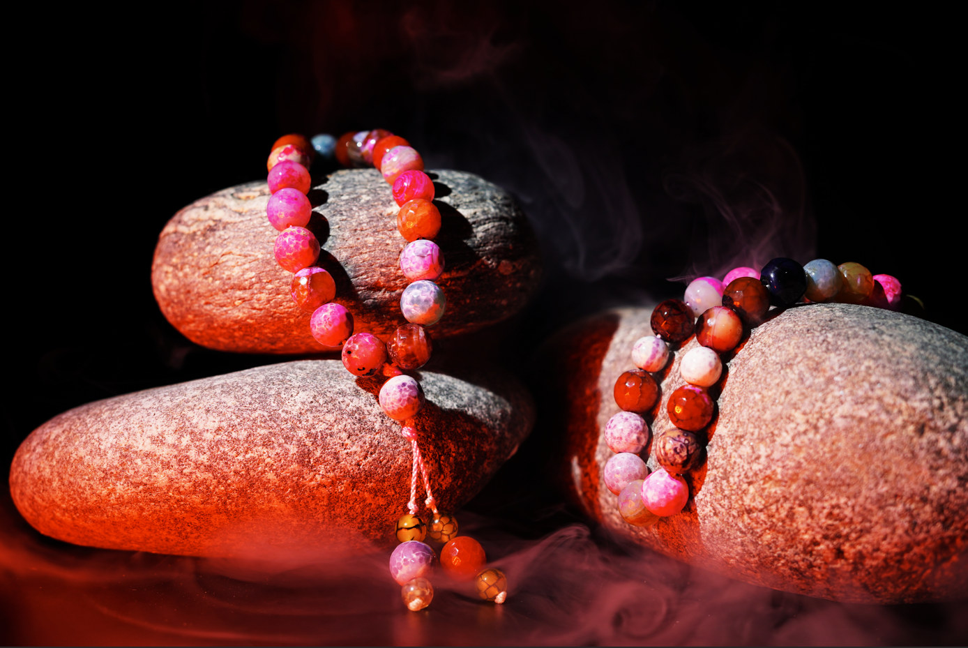 Two agate colored Tasbihs on textured stones with a dark background and mist