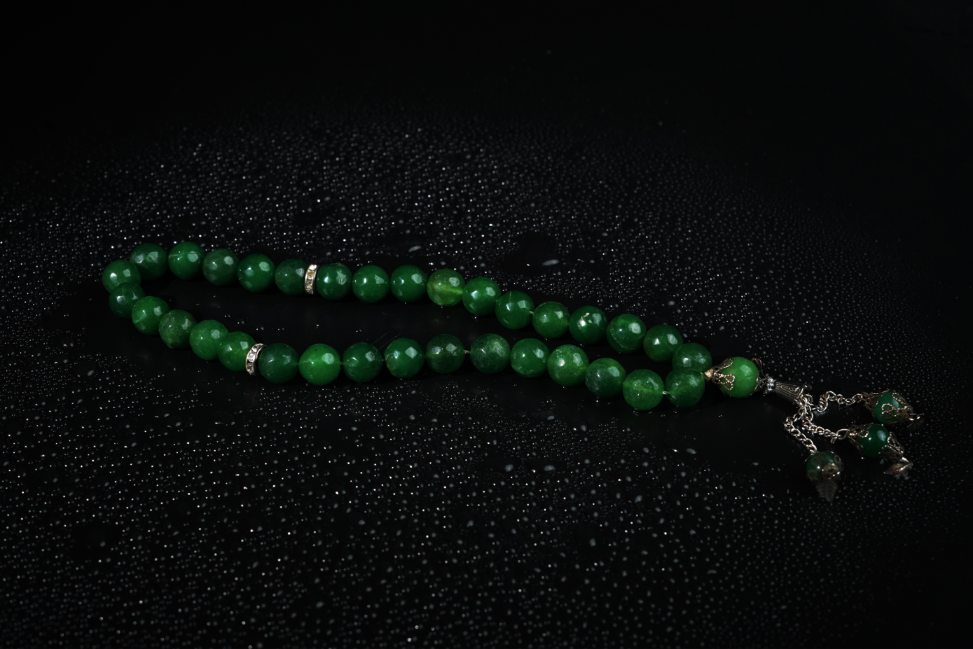 Agate green beaded Tasbih with silver tassel on black background with water droplets