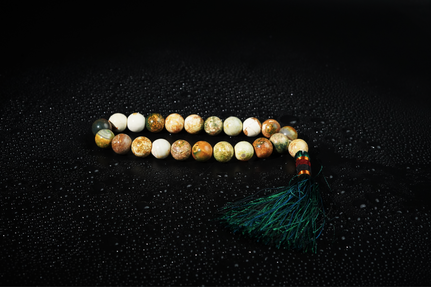 Earth-tone agate tasbih on dark backdrop with droplets